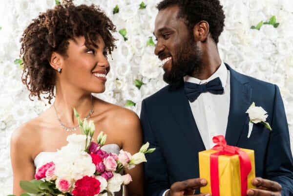 wedding festive cheerful african american bride holding fowers near happy bridegroom with present